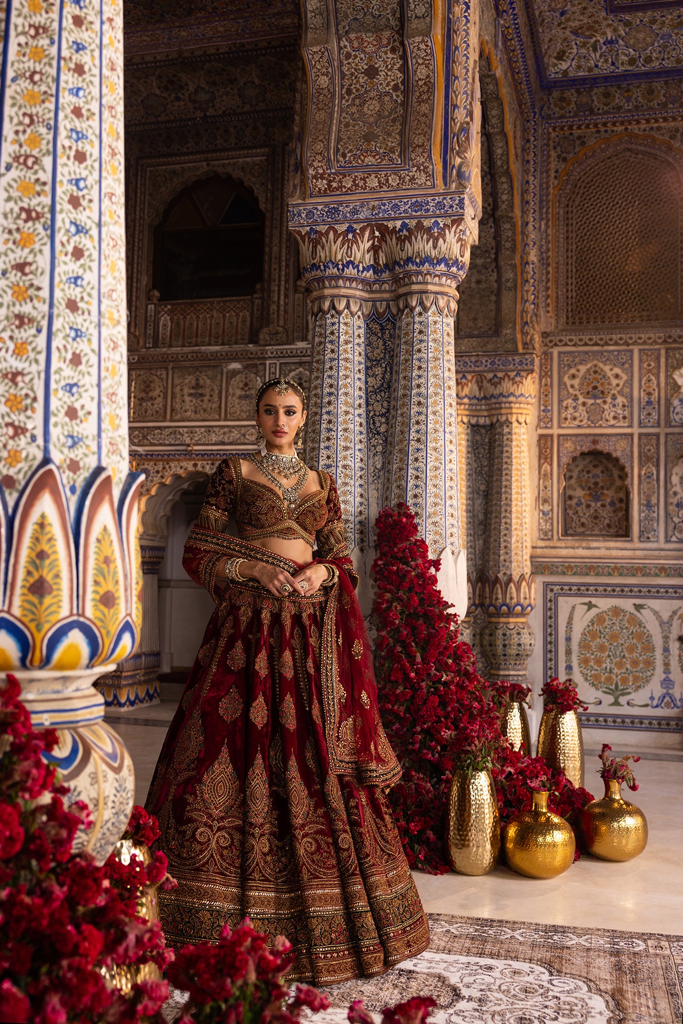 Woman in traditional attire standing in a decorated interior space with floral arrangements and decorative elements.